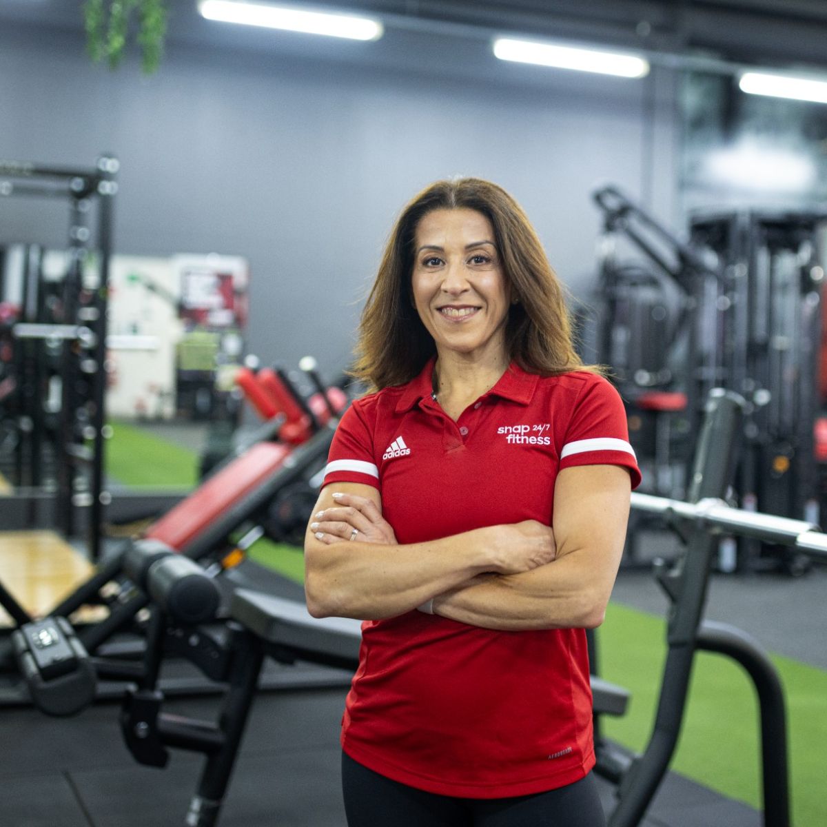 A woman wearing a Snap Fitness polo shirt posing inside the gym